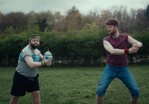 Two main characters work out in a garden holding an urn